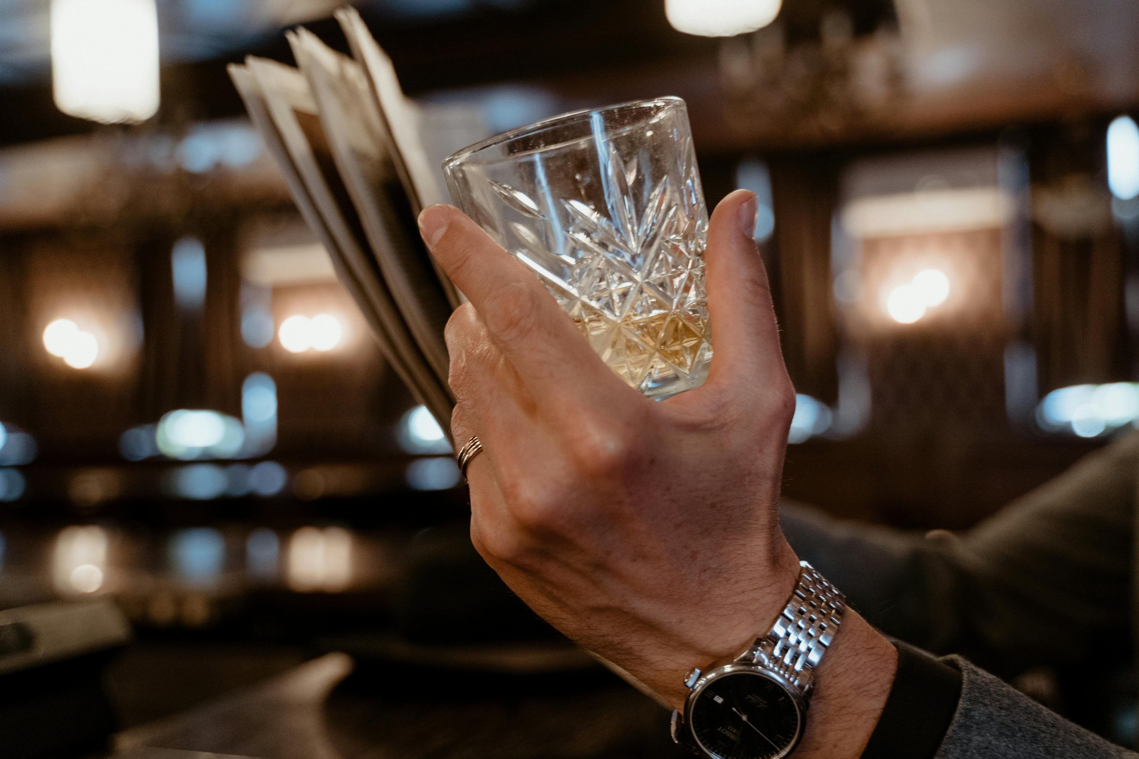 Hand holding a glass of whiskey with a blurred bar background